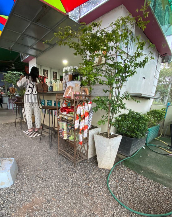 Front view of The Press Day Coffee shop in Battambang with colorful umbrellas and outdoor seating on gravel.
